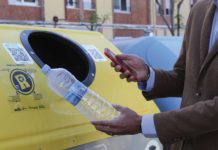 Imatge d'un contenidor groc amb una persona escanejant el codi QR abans de llençar una ampolla de plàstic